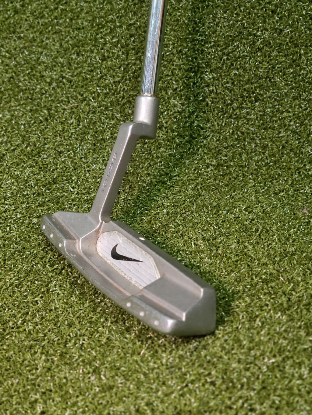 A Nike golf putter with a silver metal head and shaft, resting on green artificial turf.