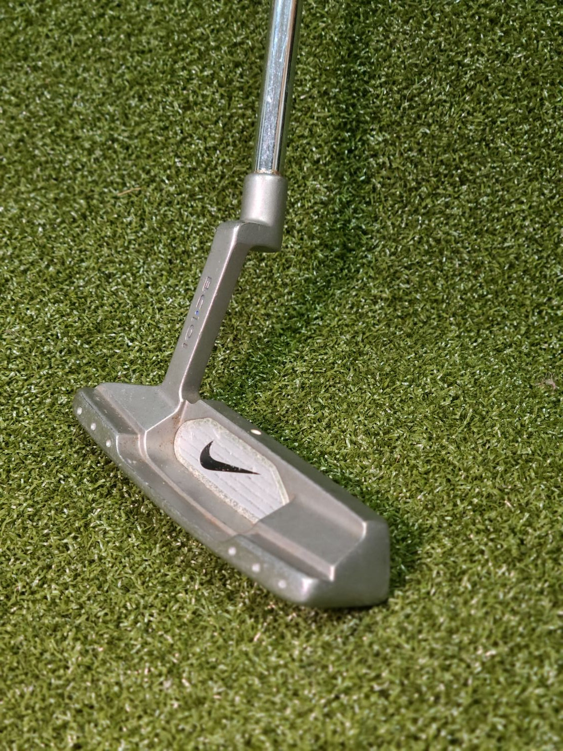A Nike golf putter with a silver metal head and shaft, resting on green artificial turf.